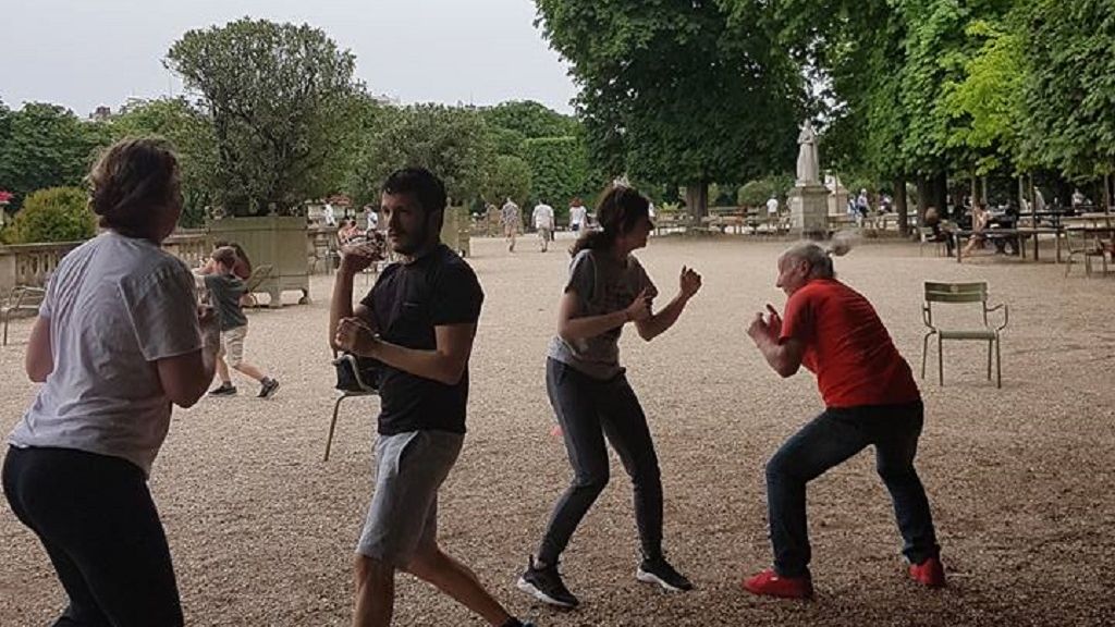 Des participants s’exercent en binôme aux mouvements de combat dans les allées du jardin.